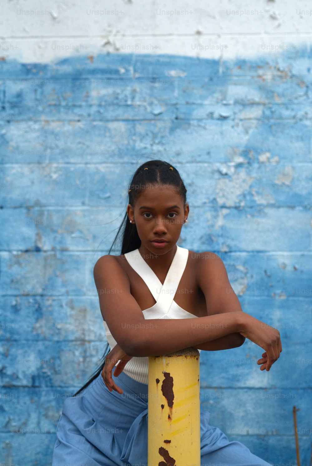 a young woman sitting on a pole in front of a blue wall