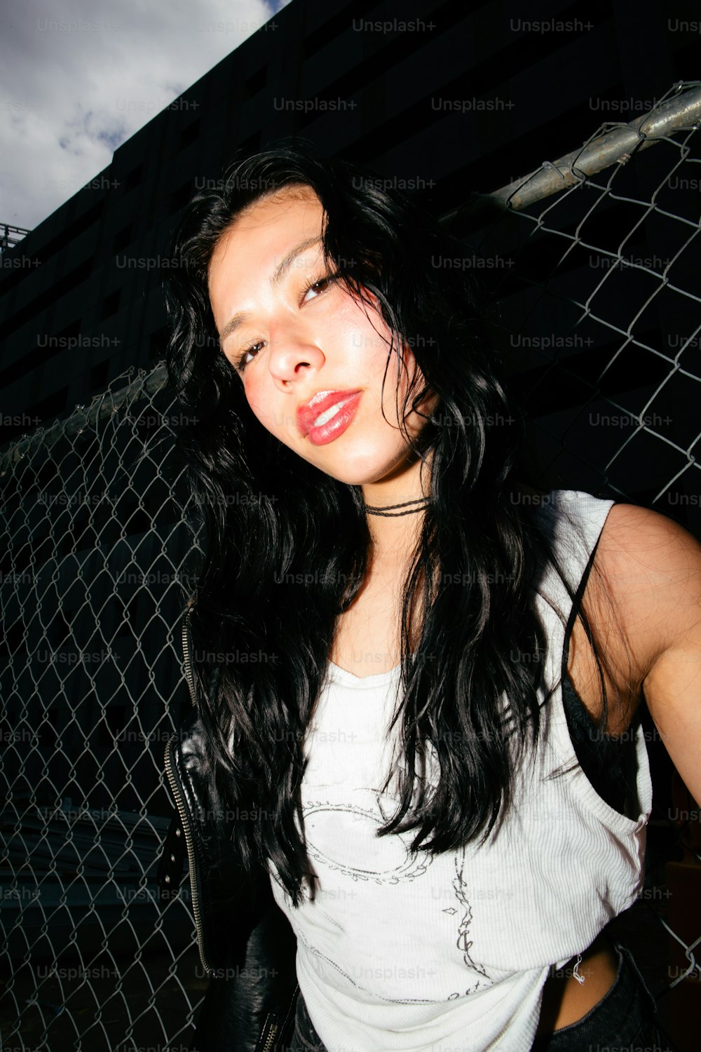 a woman with long black hair standing next to a fence