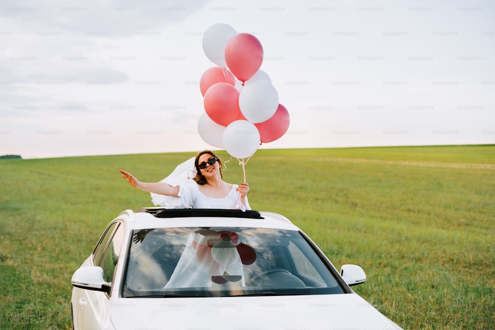 a woman sitting on top of a car holding balloons
