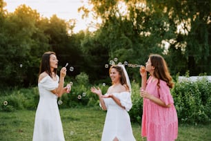 three women in dresses blowing bubbles in a field