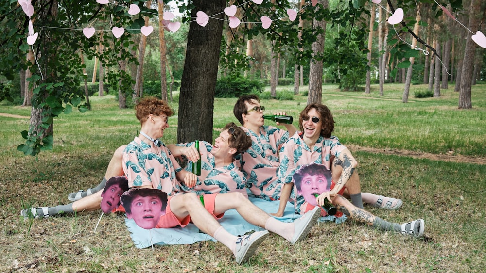 a group of people sitting on top of a blanket under a tree