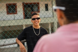 a man wearing sunglasses standing next to a fence