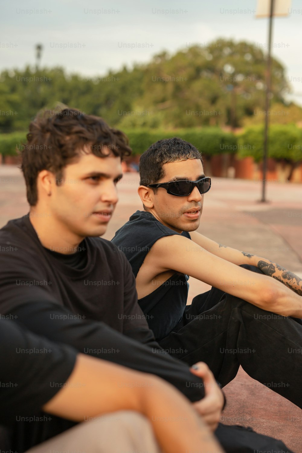 two young men sitting on the ground with their arms crossed