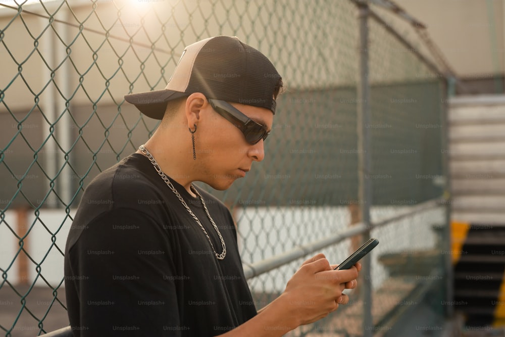 a man in a baseball cap and sunglasses looking at a cell phone