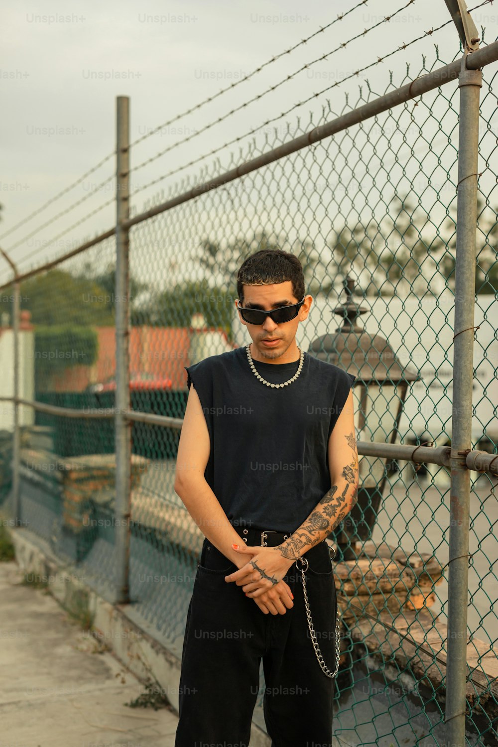 a man with a chain on his arm standing in front of a fence