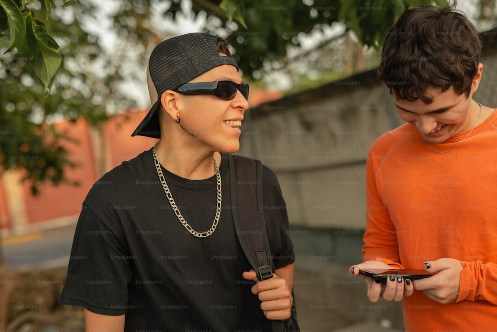 two young men standing next to each other looking at a cell phone