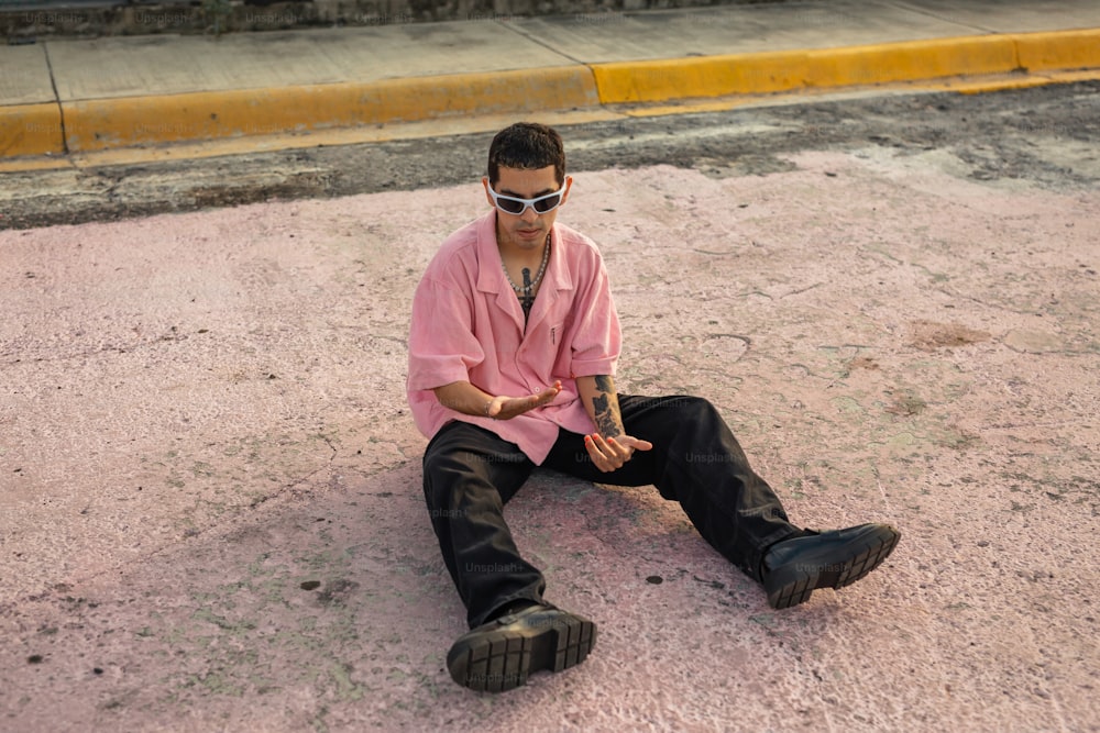 a man sitting on the ground wearing sunglasses and a pink shirt
