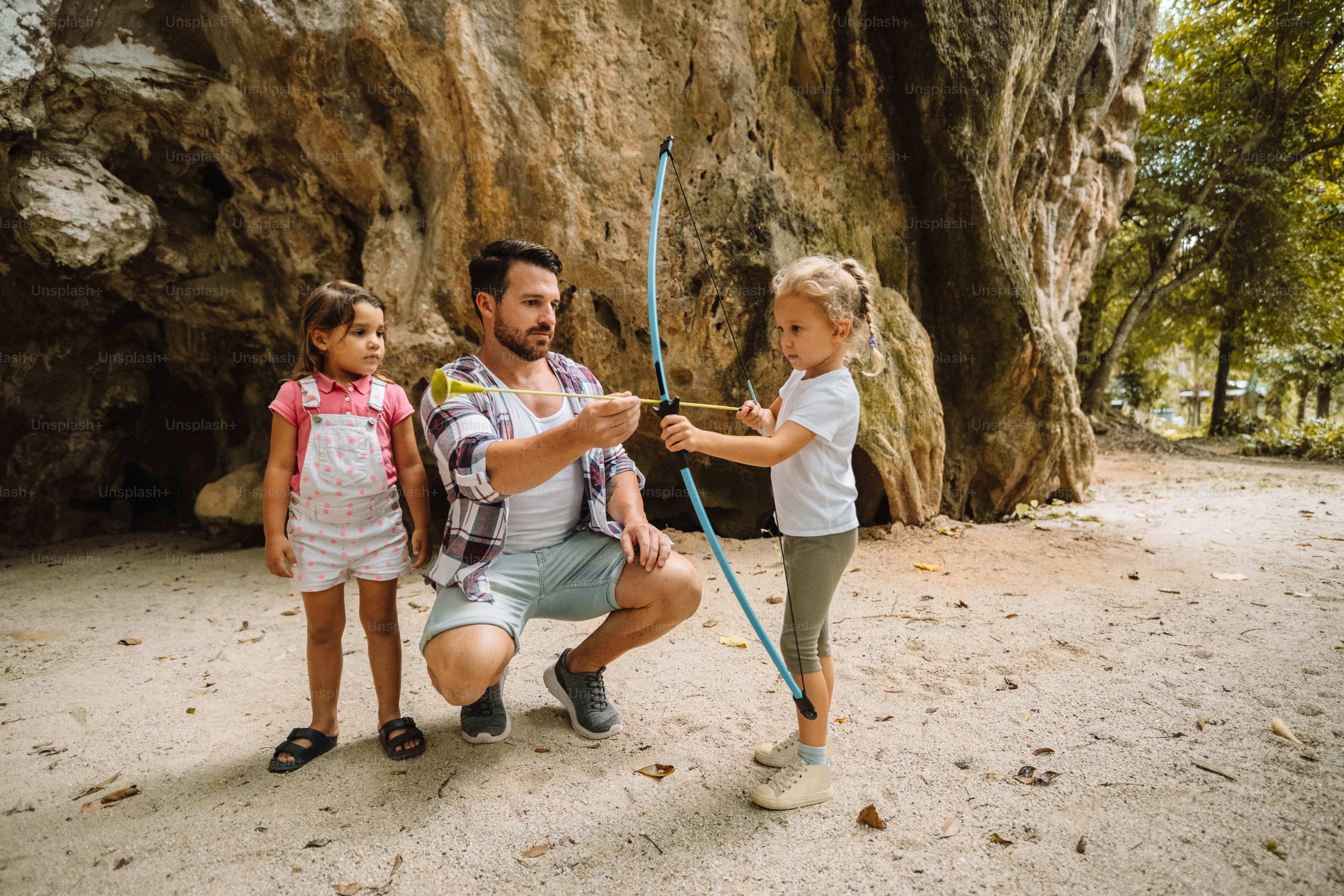 ein mann, der neben einem kleinen mädchen kniet, das pfeil und bogen hält