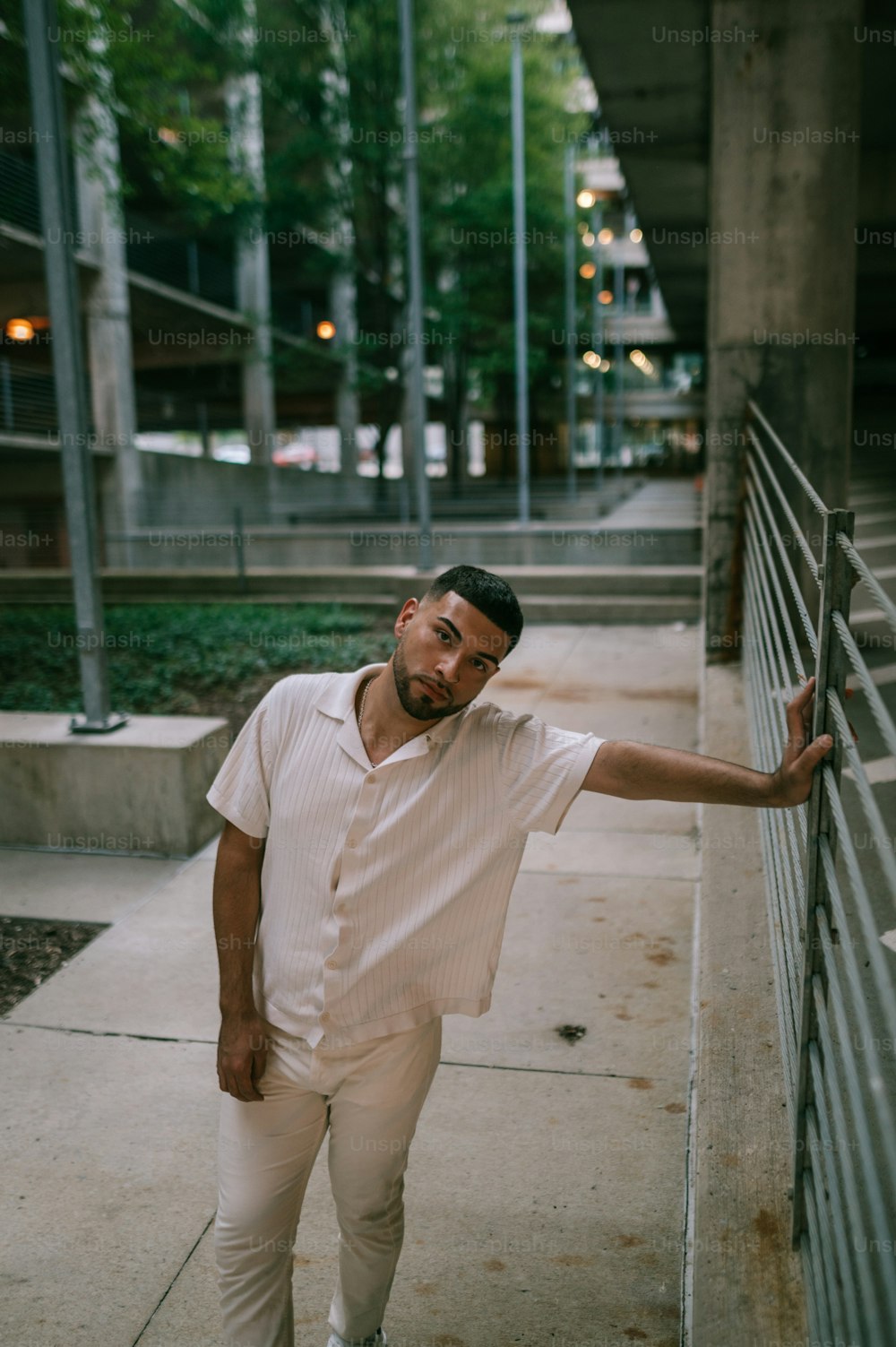 a man leaning against a fence on a sidewalk