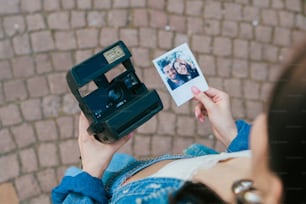 Uma mulher segurando uma câmera Polaroid e um cartão Polaroid
