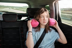 Una donna seduta sul sedile posteriore di un'auto con due cuscini rosa