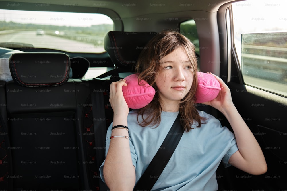 a woman sitting in the back seat of a car holding two pink pillows