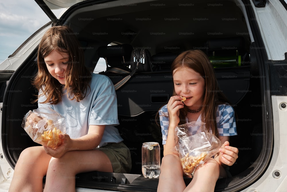 two girls sitting in the back of a car eating