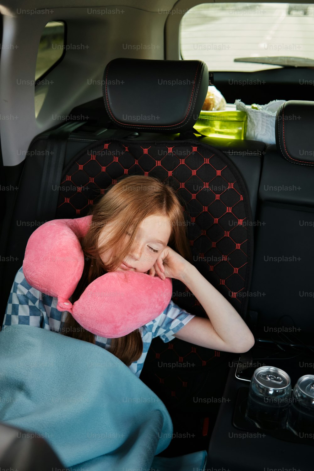 a little girl sitting in a car seat with a pink pillow