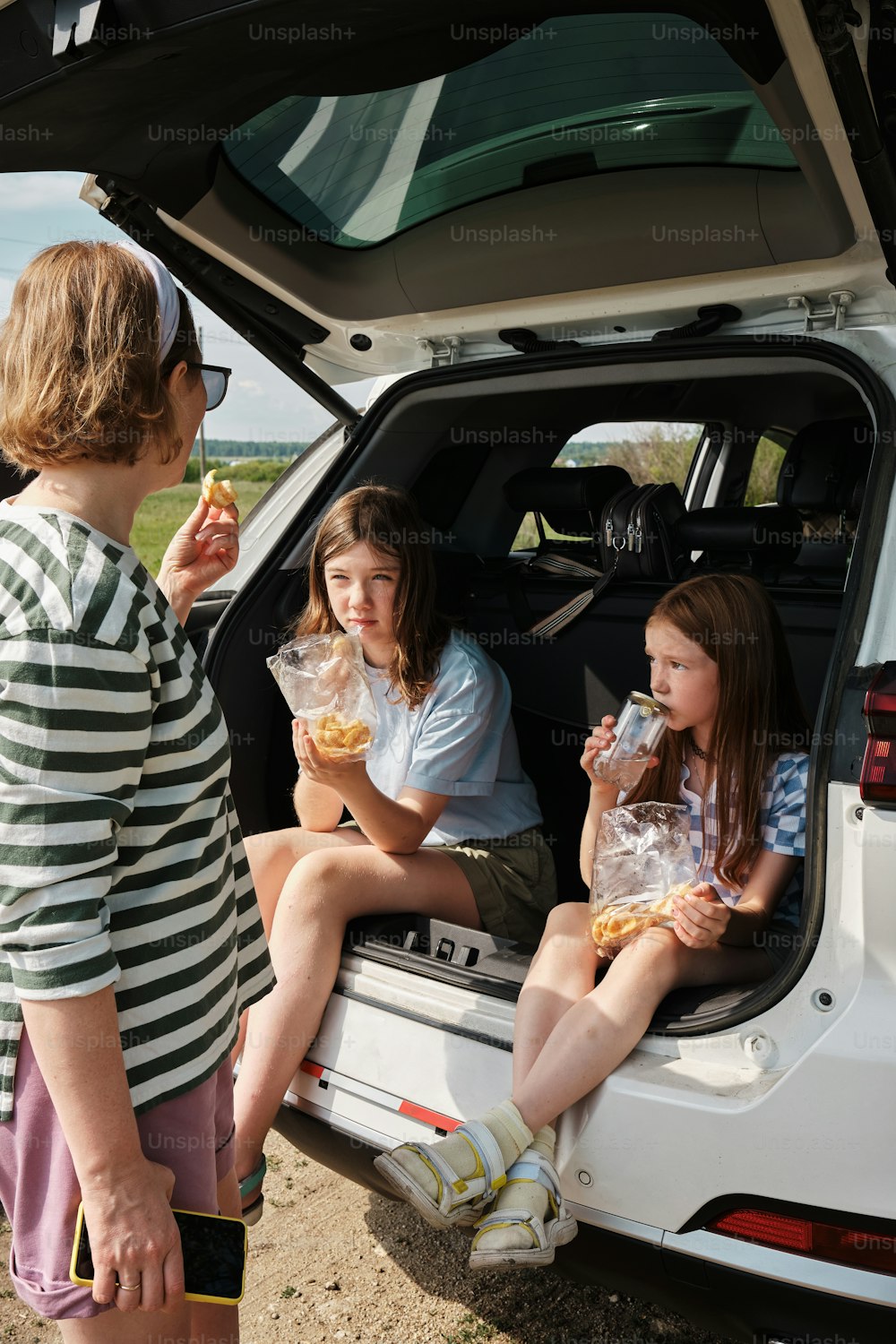 three girls sitting in the back of a car eating