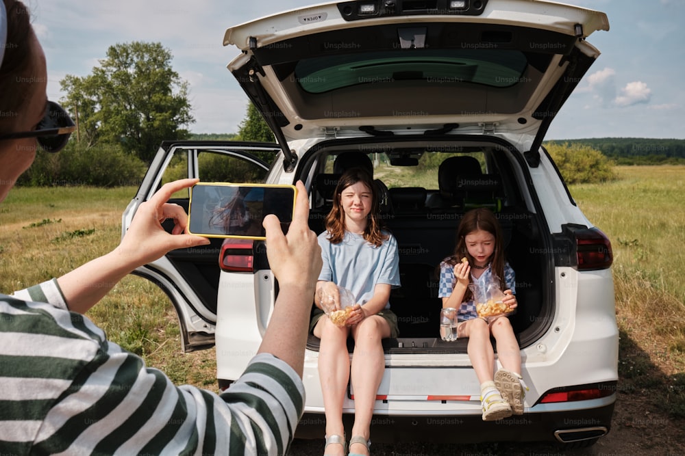 Una mujer tomando una foto de dos niñas sentadas en la parte trasera de un coche