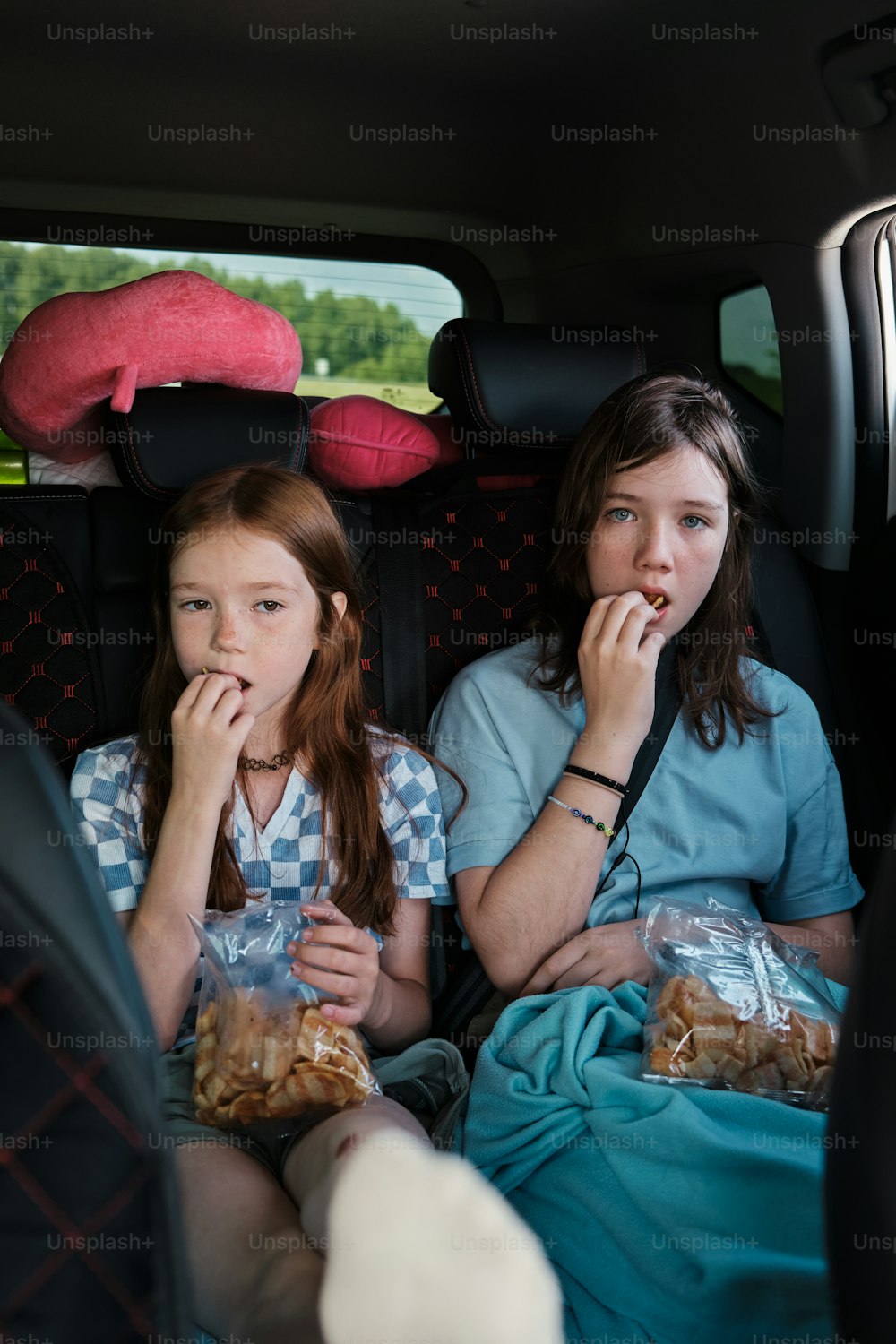 two girls sitting in the back of a car eating