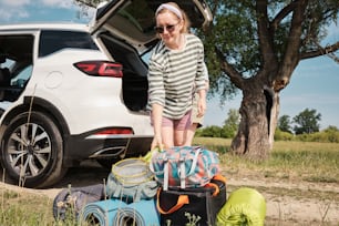 a woman standing next to a car with luggage in the trunk