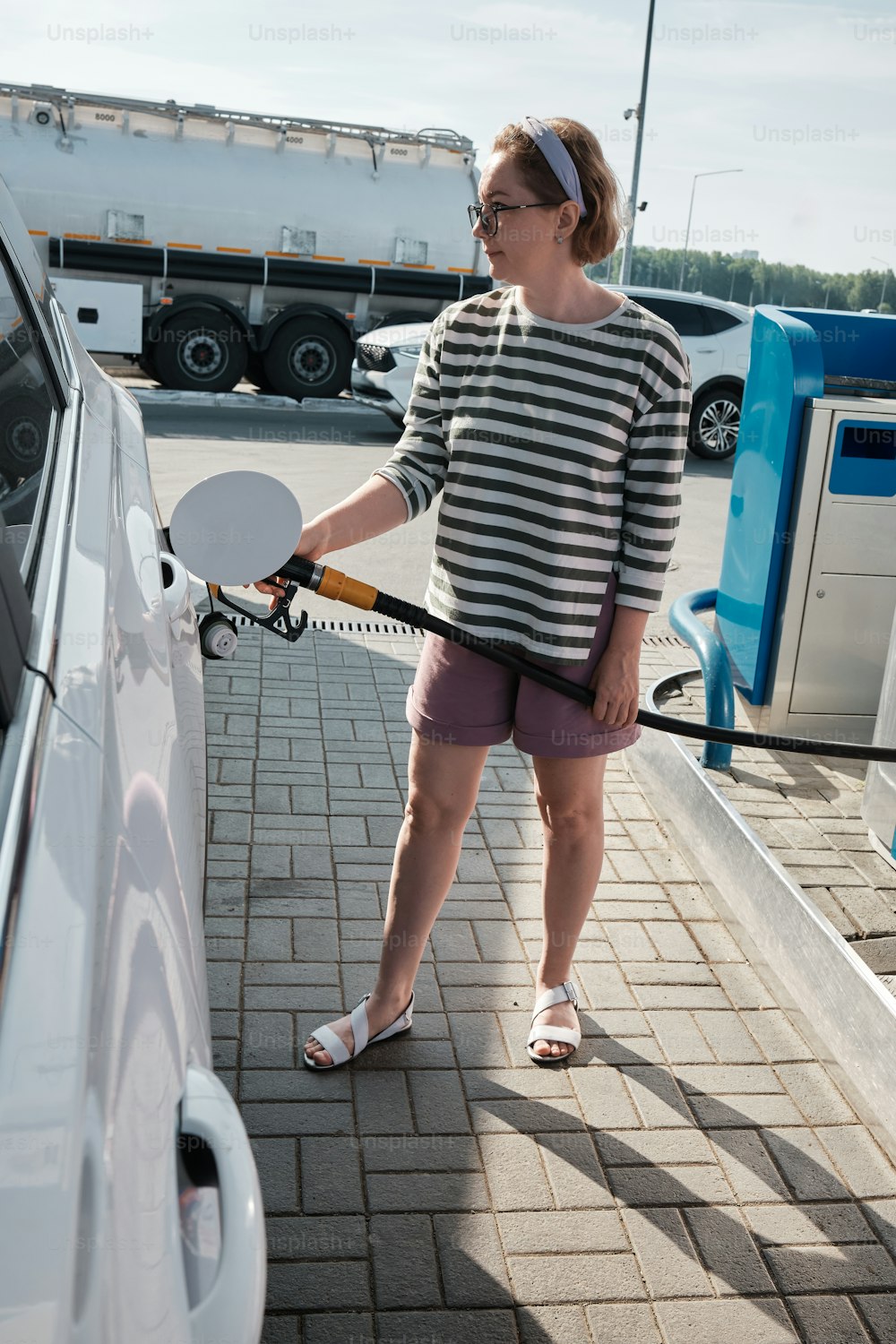 a woman pumping gas into her car at a gas station