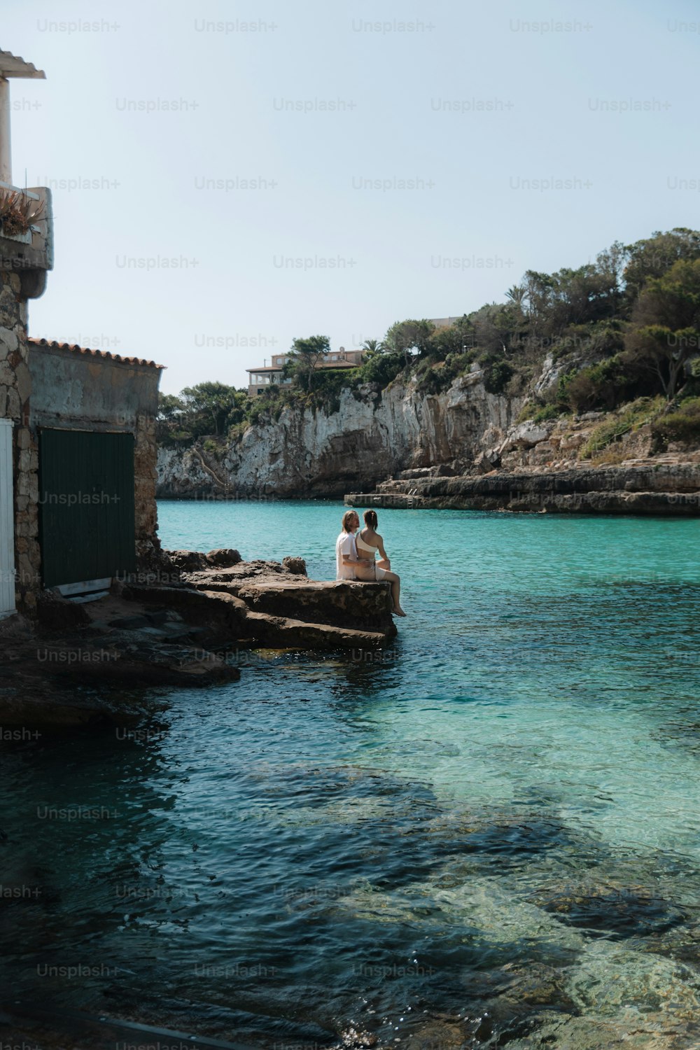 two people sitting on a rock in the water