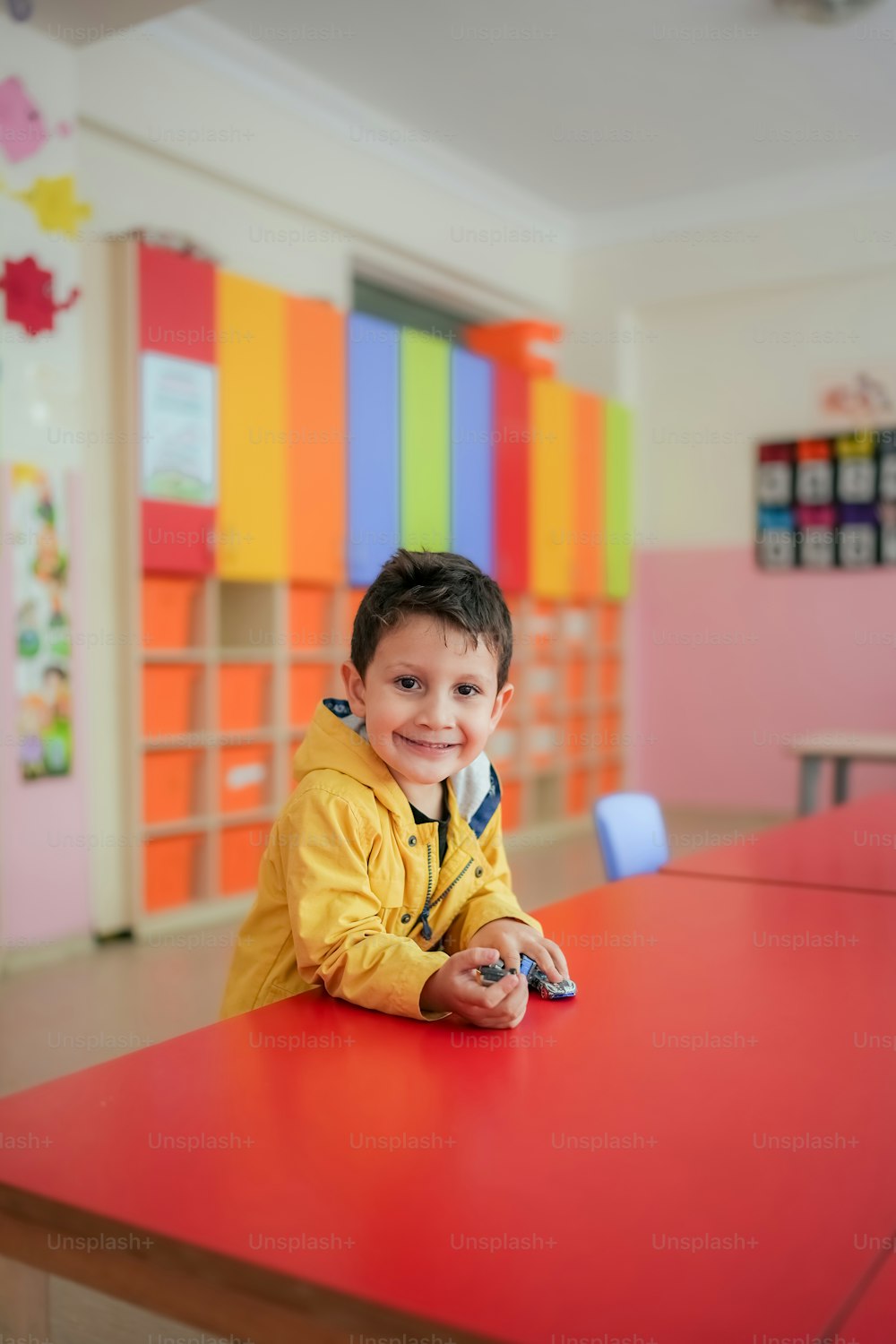 a young boy sitting at a red table in a classroom