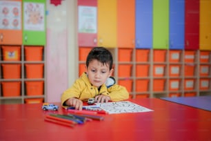 a little boy sitting at a table with some crayons