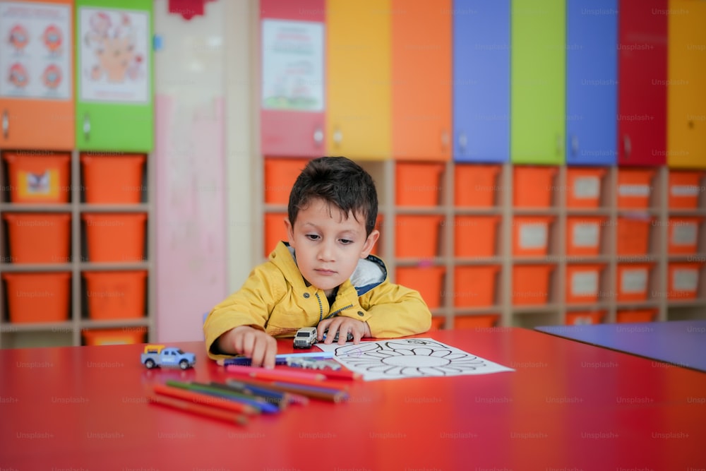 um garotinho sentado em uma mesa com alguns lápis de cor