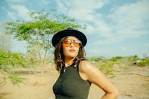 a woman wearing a hat and sunglasses standing in a field