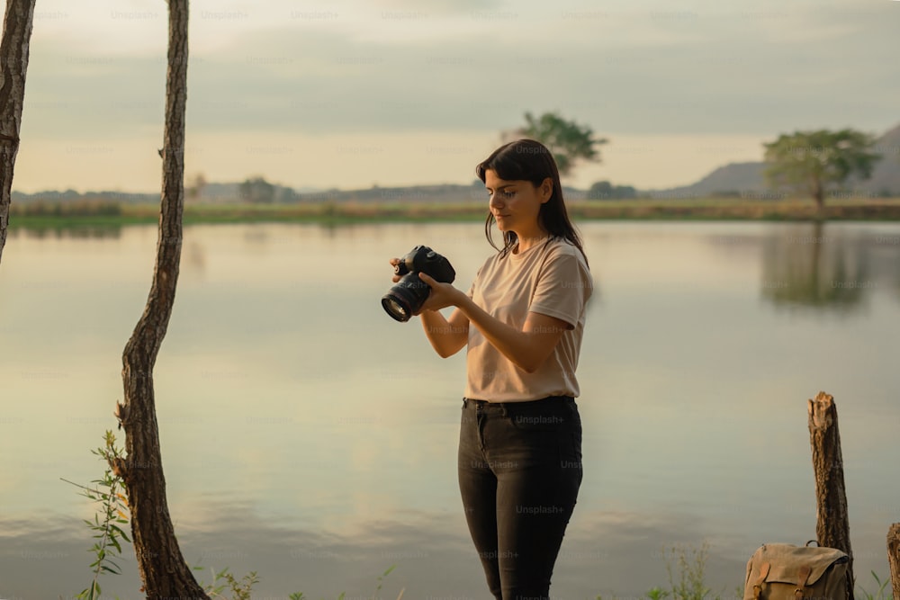 uma mulher segurando uma câmera perto de um corpo de água