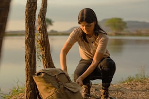 Una mujer se agacha junto a una mochila junto a un lago