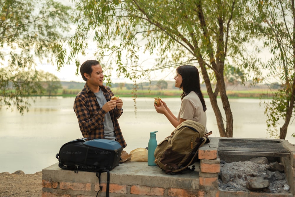 a man and a woman sitting on a brick wall next to a lake