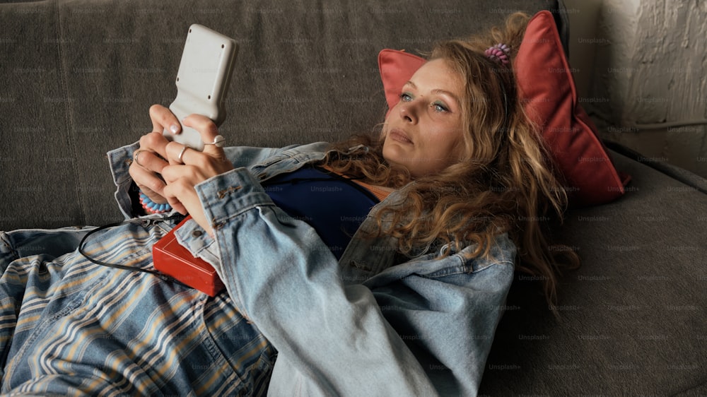 Una donna che si trova su un divano che tiene un telefono cellulare
