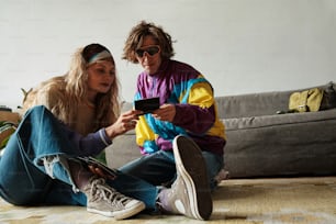 한 남자와 한 여자가 바닥에 앉아 휴대폰을 보고 있다