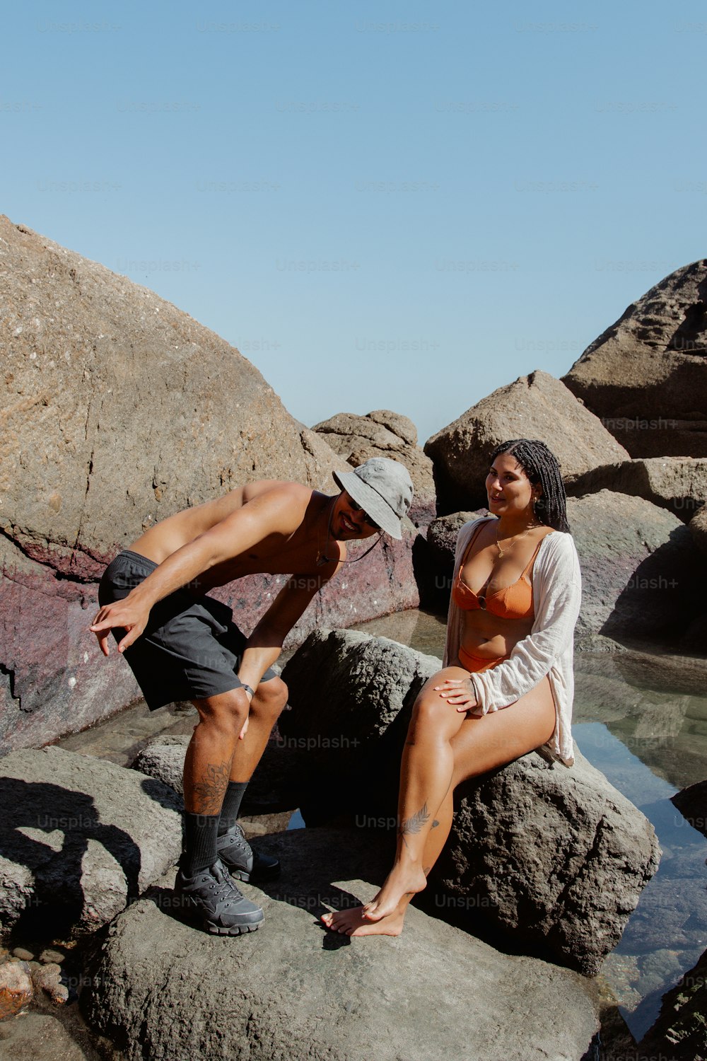 a man and a woman sitting on rocks near water