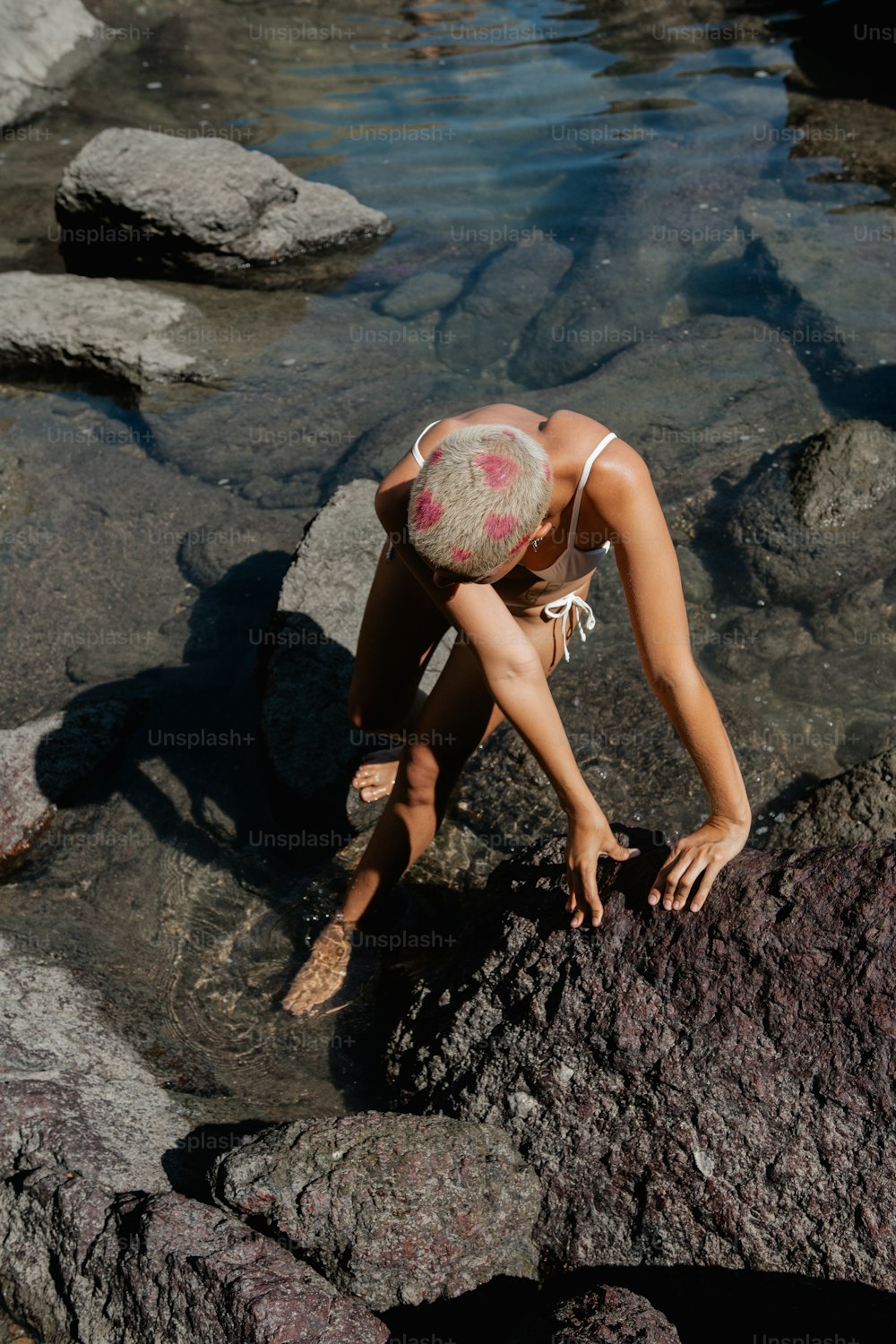 a woman in a bathing suit is on a rock by the water