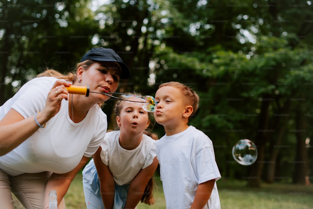 a woman and two children blowing bubbles in a park