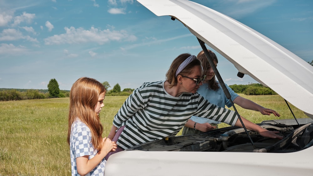 a woman and a little girl looking under the hood of a car
