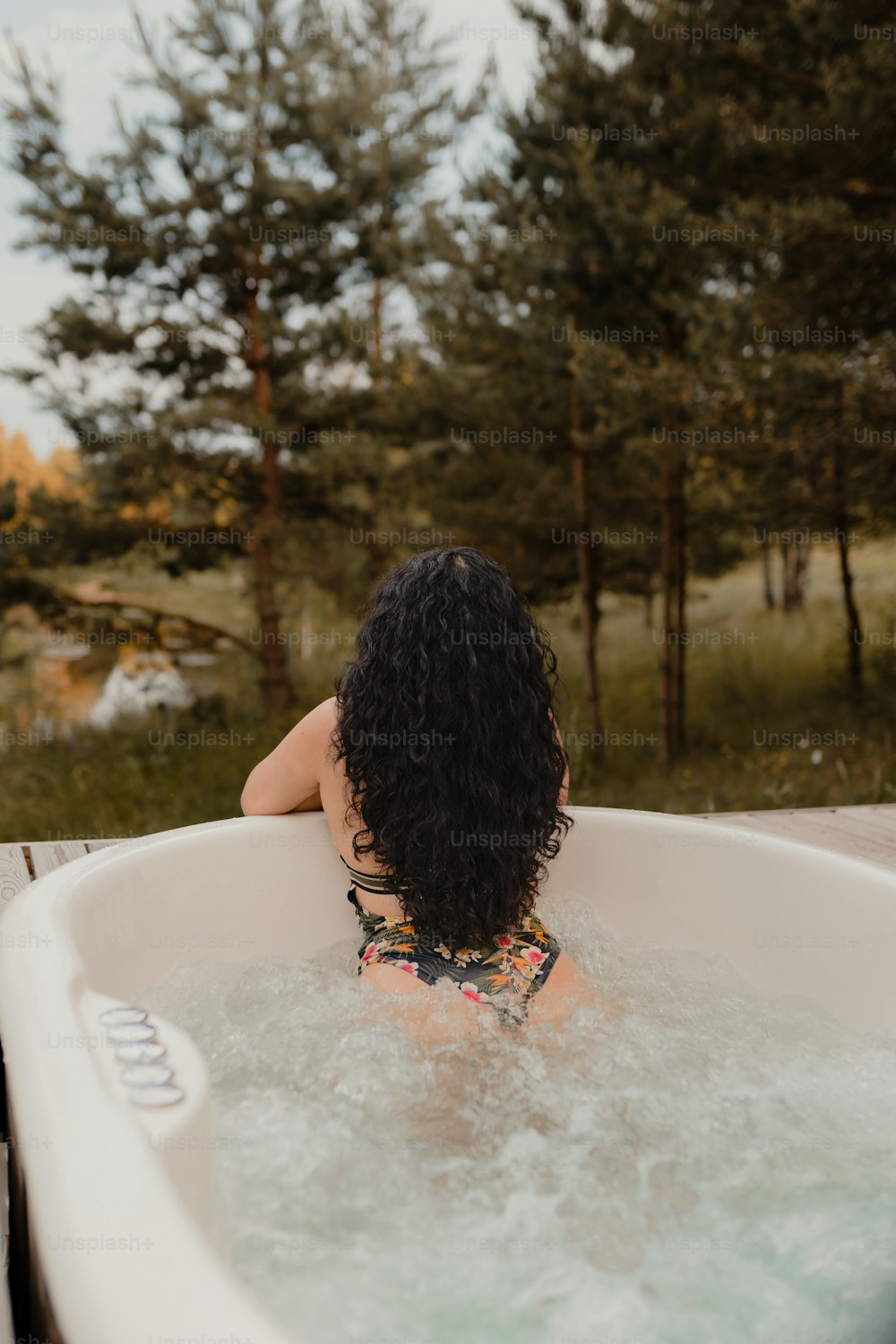 a woman sitting in a bathtub with trees in the background