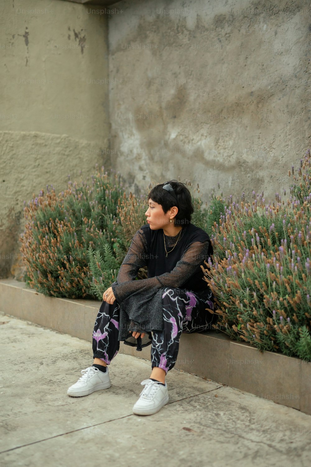 a woman sitting on a curb next to a plant