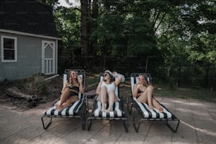 three women lounging on lounge chairs in front of a house