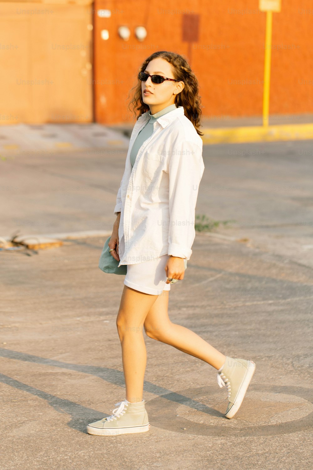 a woman walking across a parking lot wearing sunglasses