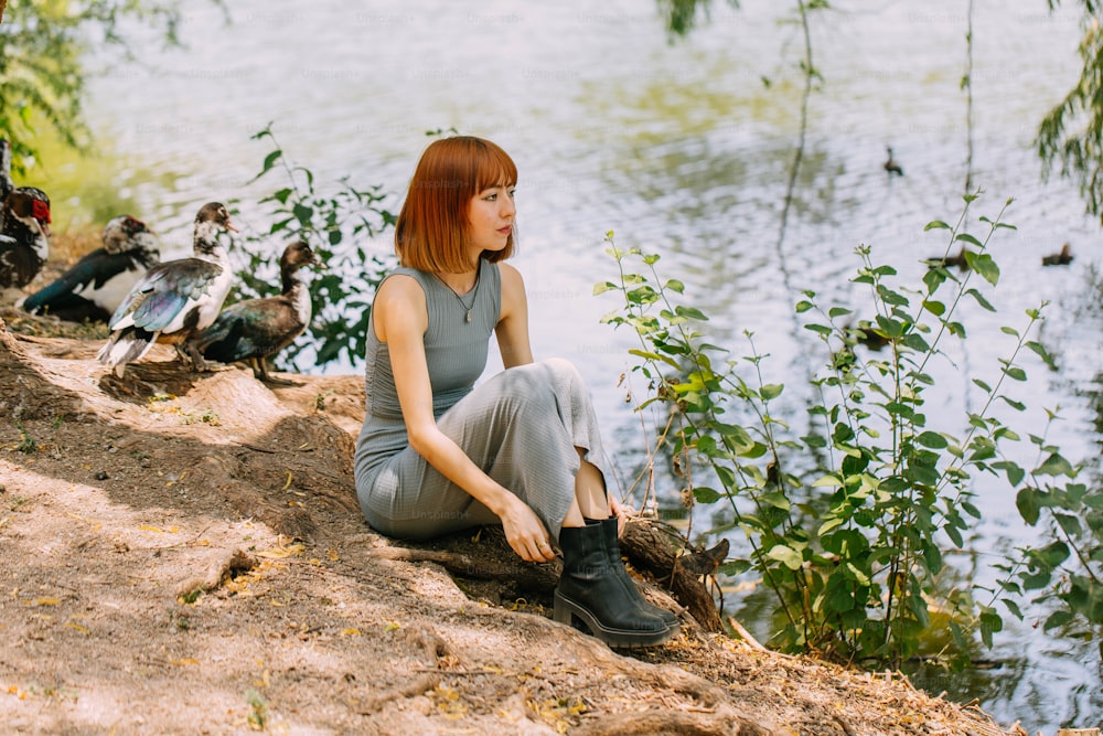 Una mujer sentada en una roca junto a un cuerpo de agua