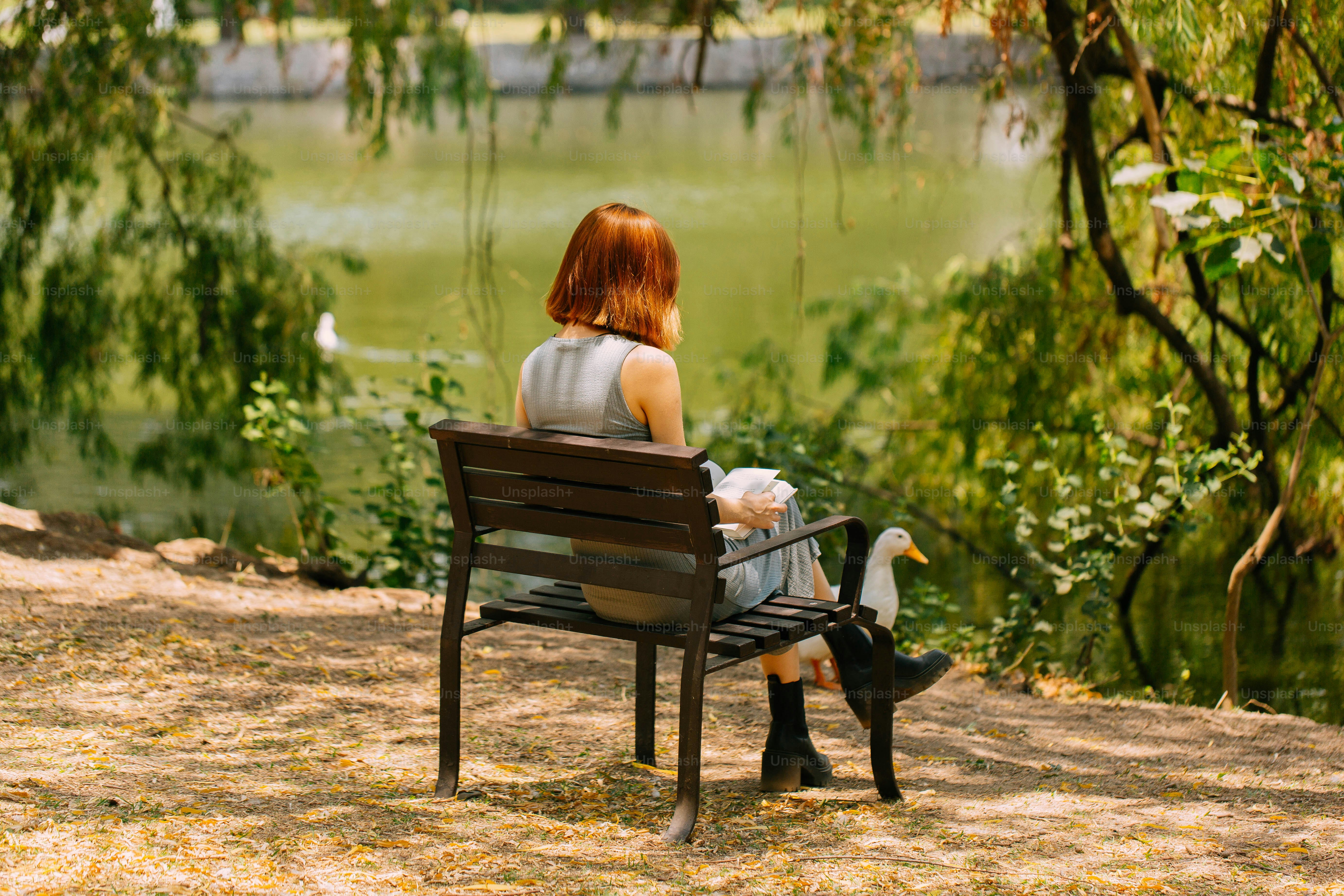 a woman sitting on a bench next to a lake