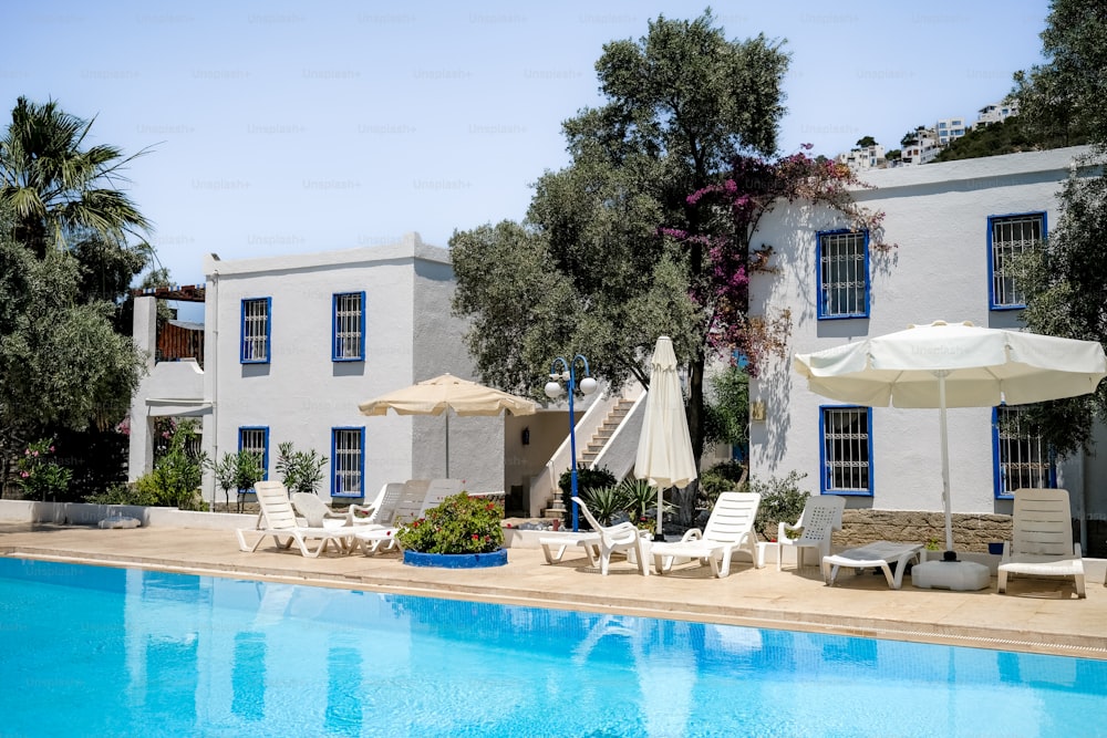 a pool with chairs and umbrellas next to a house