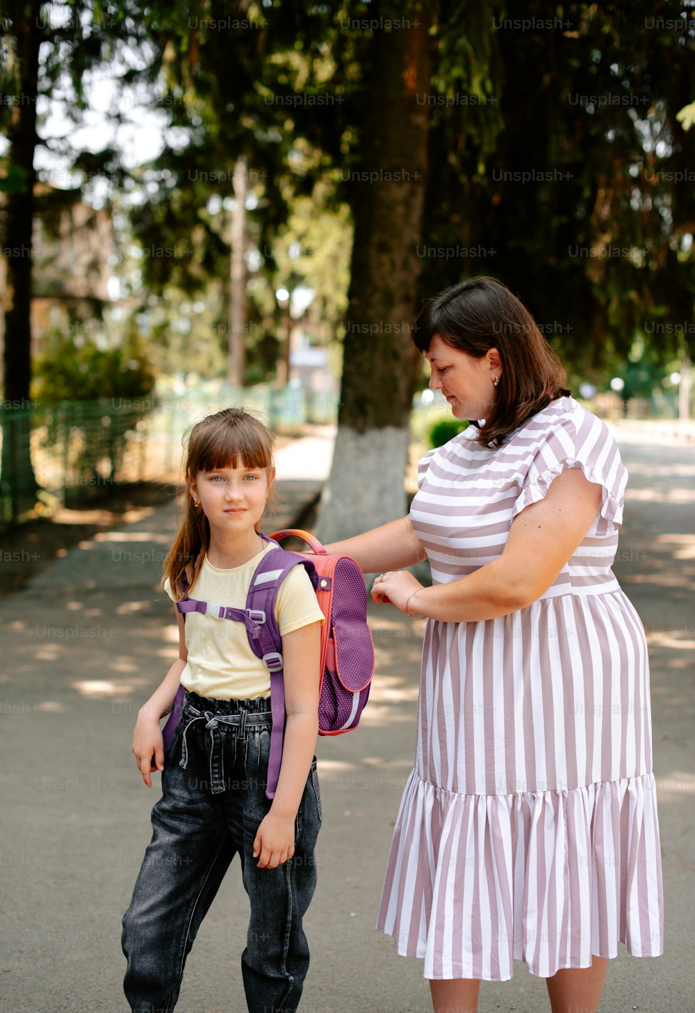 Eine Frau hilft einem kleinen Mädchen mit ihrem Rucksack