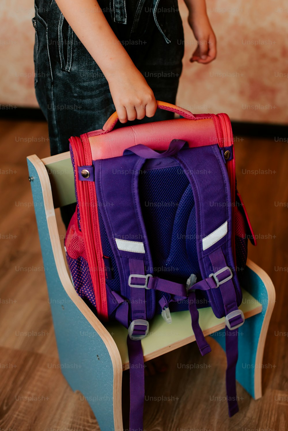 a little girl holding a purple and red backpack