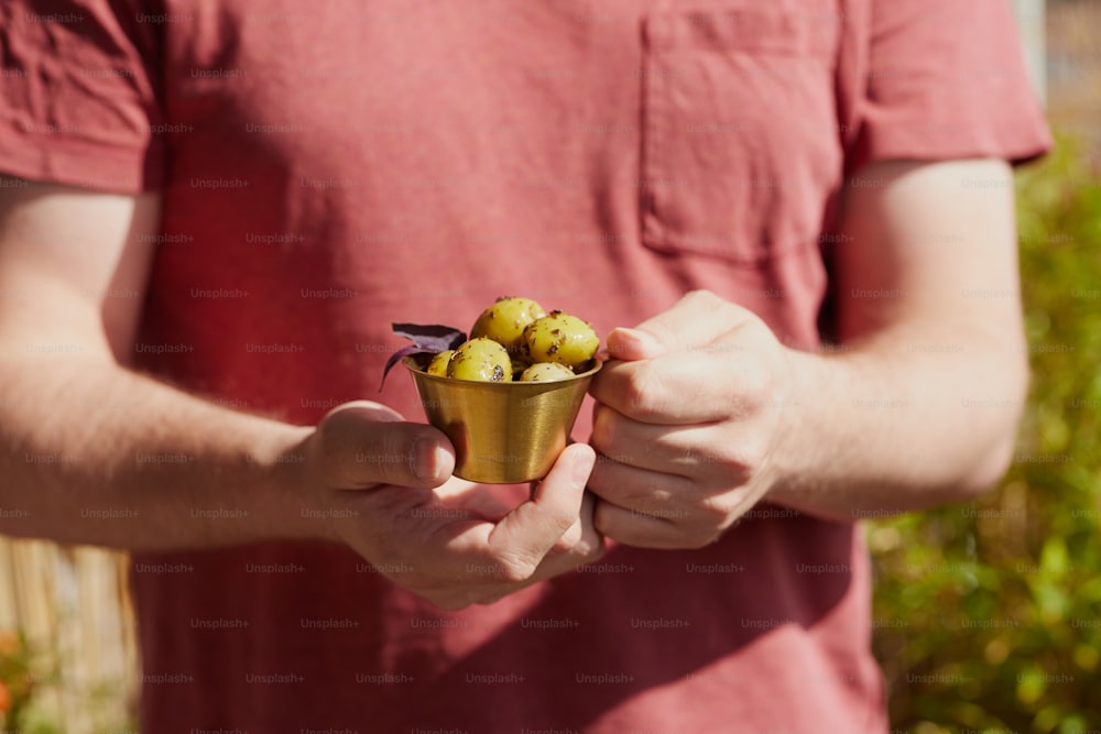 Un hombre sosteniendo una pequeña taza llena de fruta