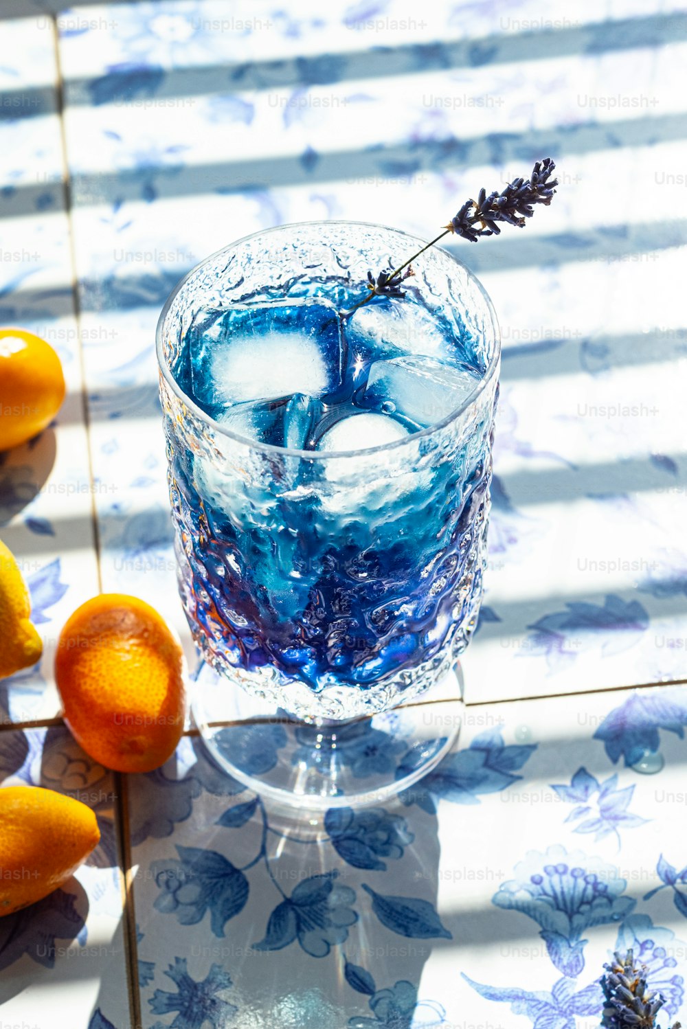 a glass filled with blue liquid next to oranges