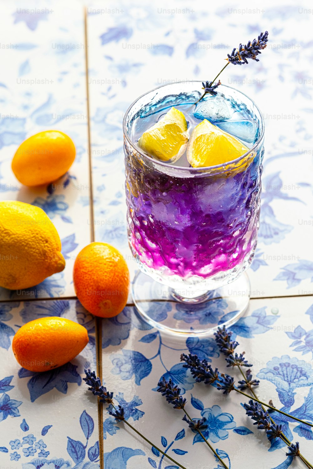 Un vaso lleno de líquido púrpura junto a limones y lavanda