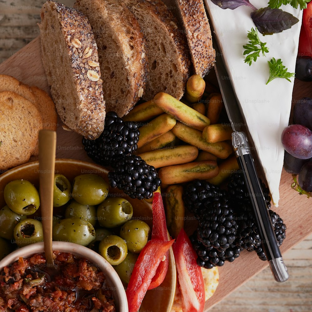 a wooden cutting board topped with bread, olives, breadsticks, and